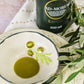 Imagen de botella aceite de oliva virgen extra temprano (AOVE Temprano) Ad-Morum y un plato al lado mostrando el color del propio aceite.
