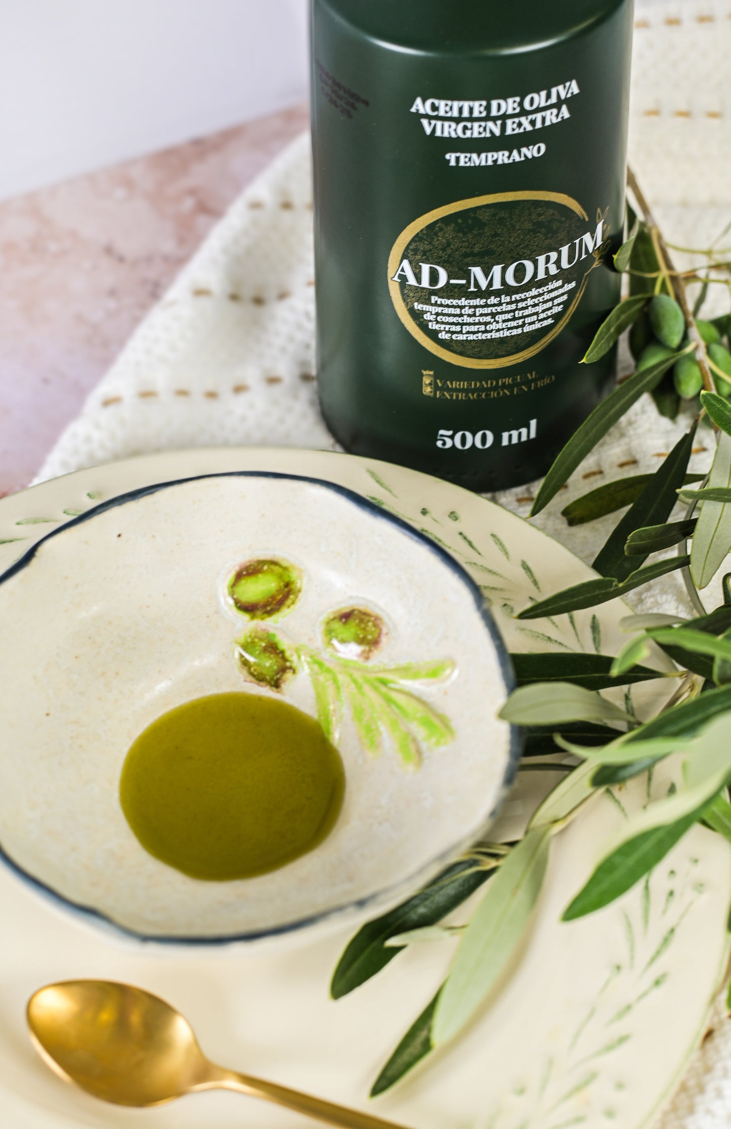 Imagen de botella aceite de oliva virgen extra temprano (AOVE Temprano) Ad-Morum y un plato al lado mostrando el color del propio aceite.